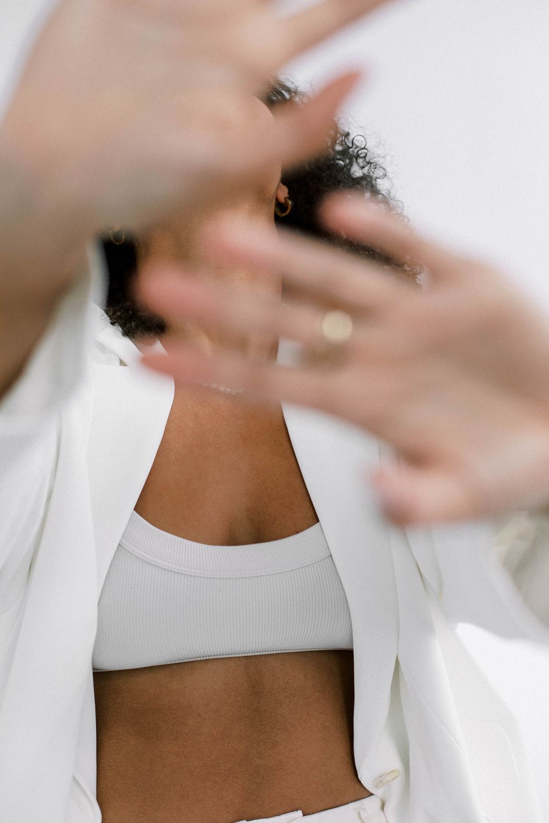 A woman in a white suit raising a hand toward the camera, face turned away.